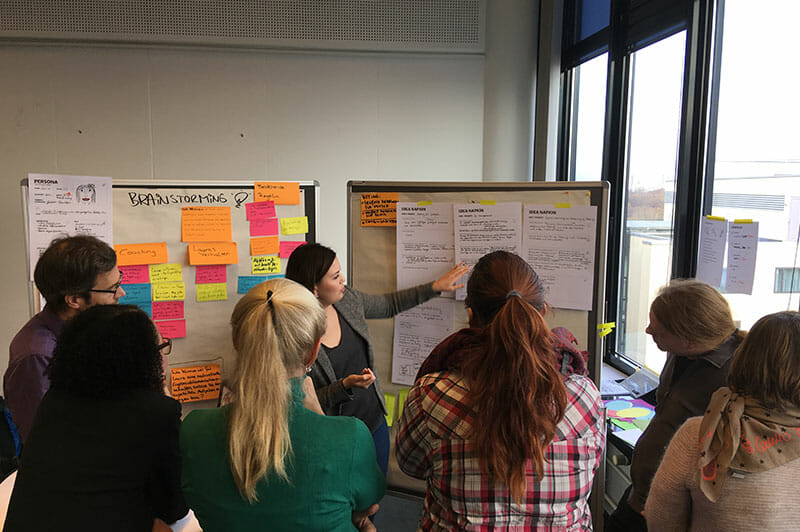 Workshopteilnehmer schauen auf ein Whiteboard während ein Coach darauf zeigt